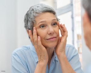 Older women with short grey hair looking in the mirror examining her eye wrinkles