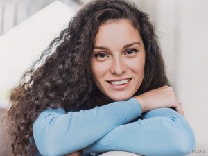 Young woman with dark curly hair resting her chin on her crossed arms