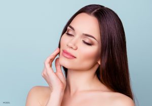 Woman with bare shoulders and eyes closed holding her hand to her smooth face