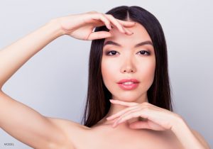 Asian women with defining cheek bones and framing her hands around her youthful face