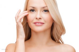 Blonde caucasian woman with bare shoulders holing her finger to her eyes
